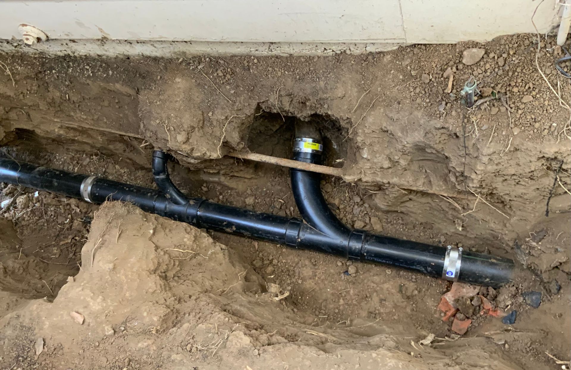Black plumbing pipes in a dirt trench, likely a sewer connection.