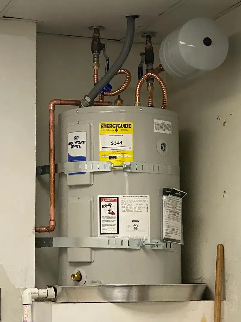 Water heater in a utility closet, with copper pipes, a thermal expansion tank, and a metal drip pan.