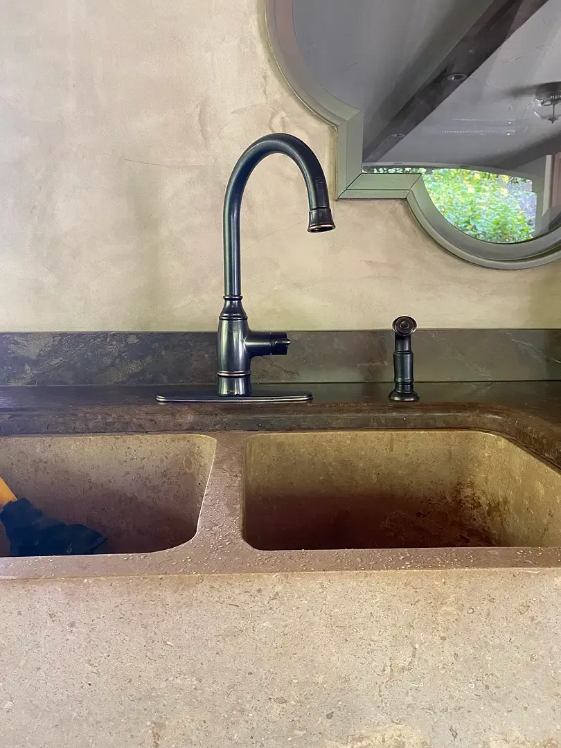 Dark faucet and soap dispenser on a stone sink, set against a textured wall.