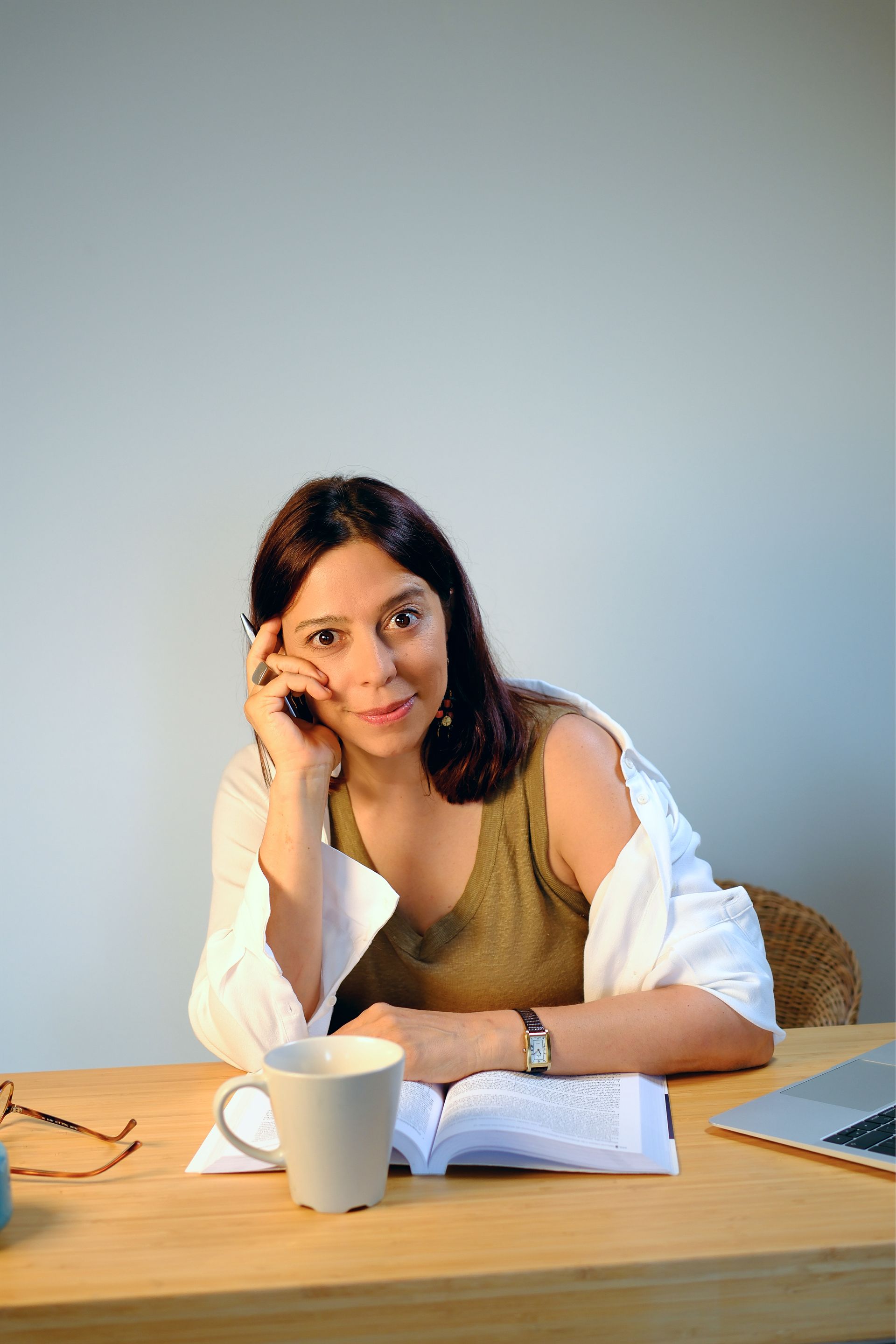 Mulher sentada à mesa, apoiada na mão e olhando para a câmera.