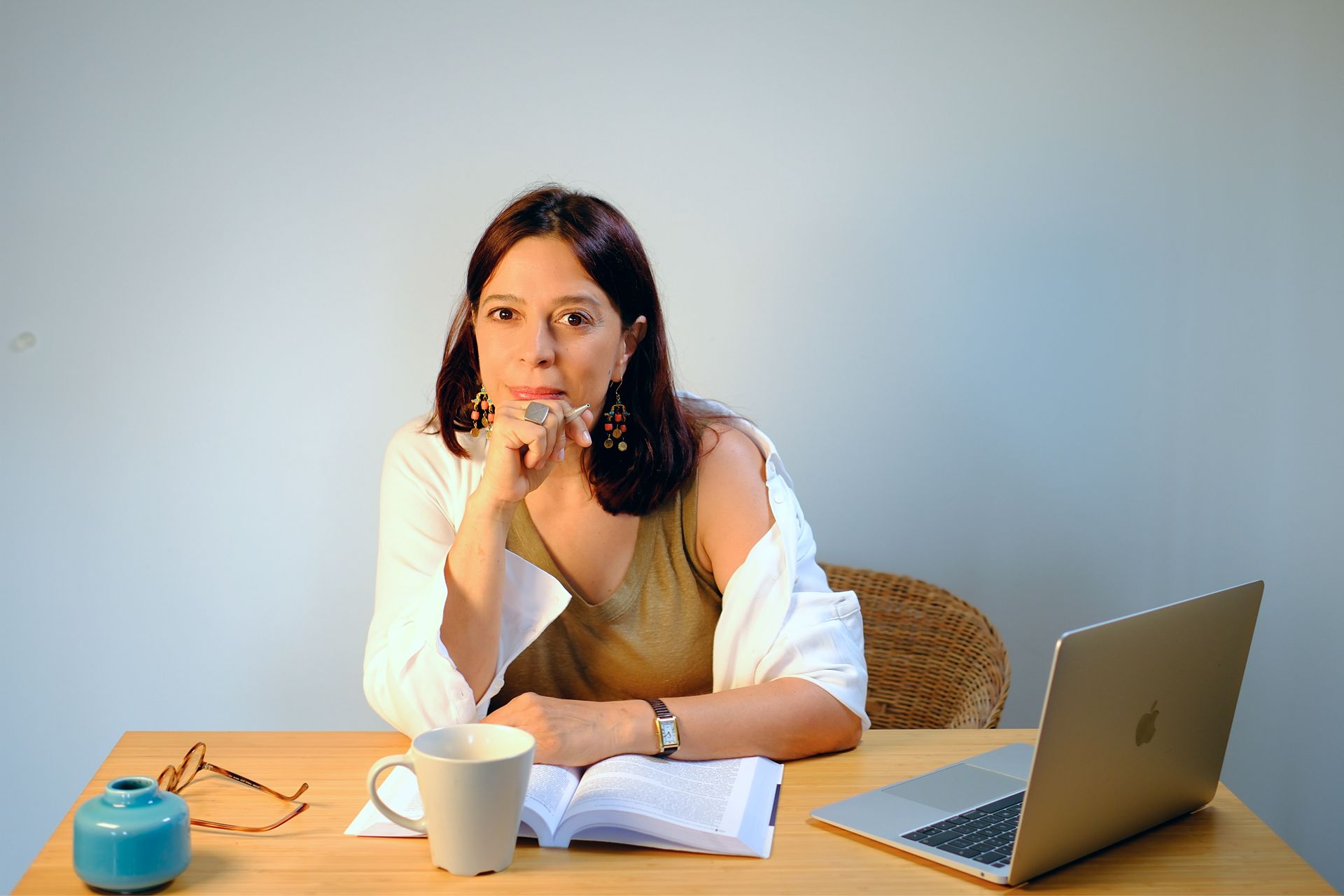 Mulher sentada à mesa, apoiada na mão e olhando para a câmera. 