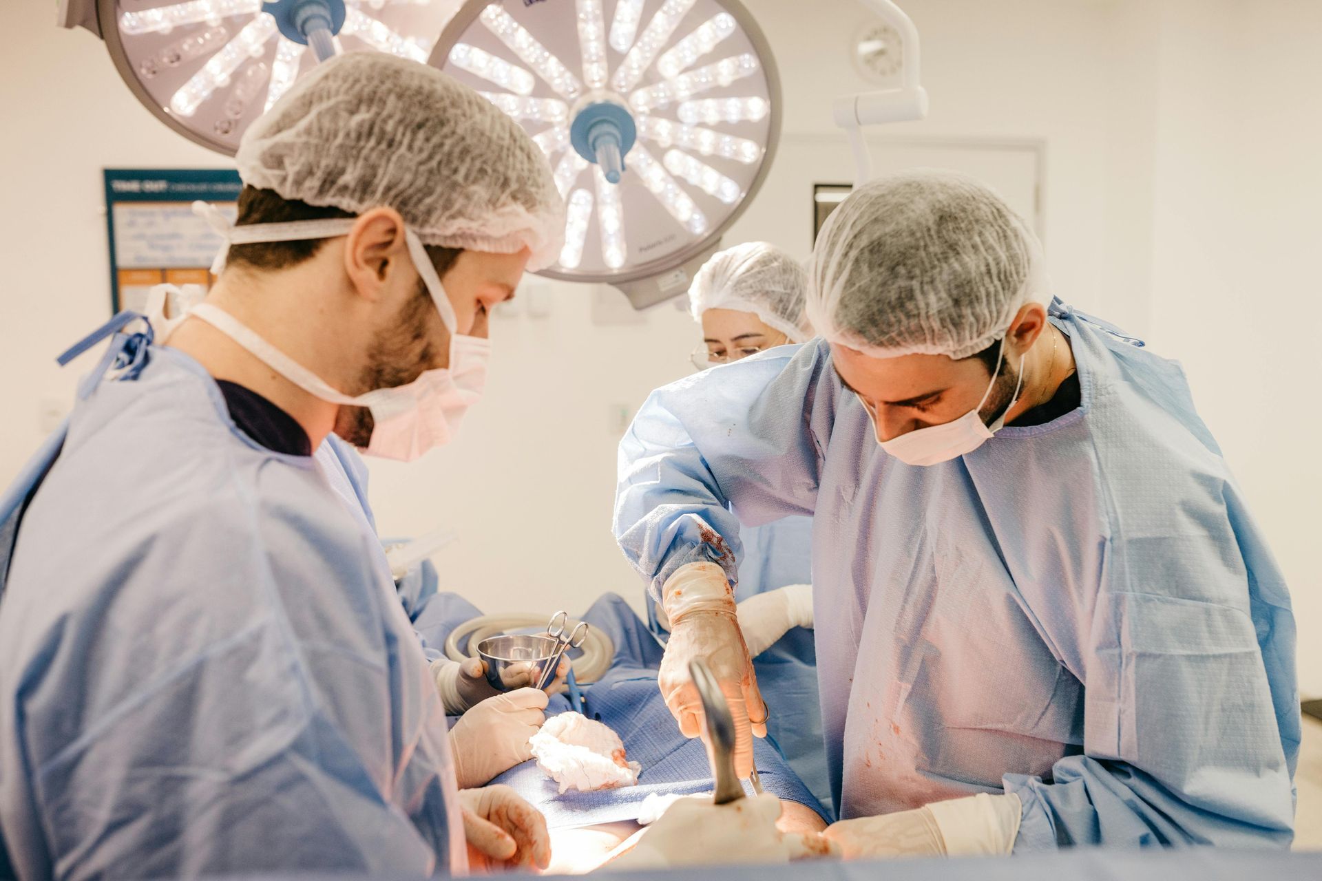 Equipe médica de uniforme azul e máscaras operando em uma sala cirúrgica estéril, focada em um paciente.