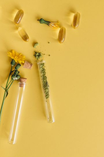 Fundo amarelo com cápsulas, tubos de ensaio com substância verde moída e flores amarelas.