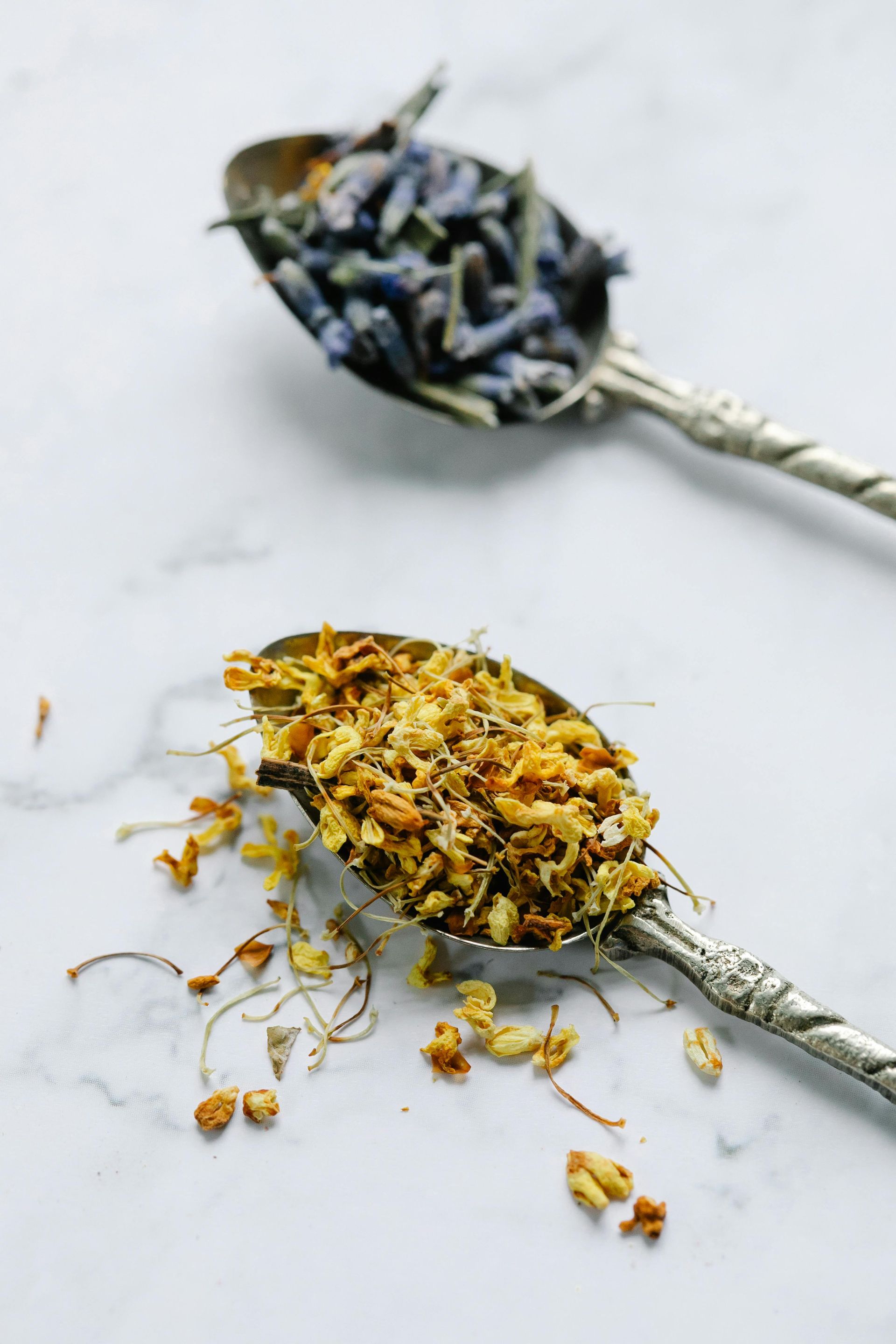 Duas colheres de prata ornamentadas com ervas secas, uma de lavanda e uma de camomila, 