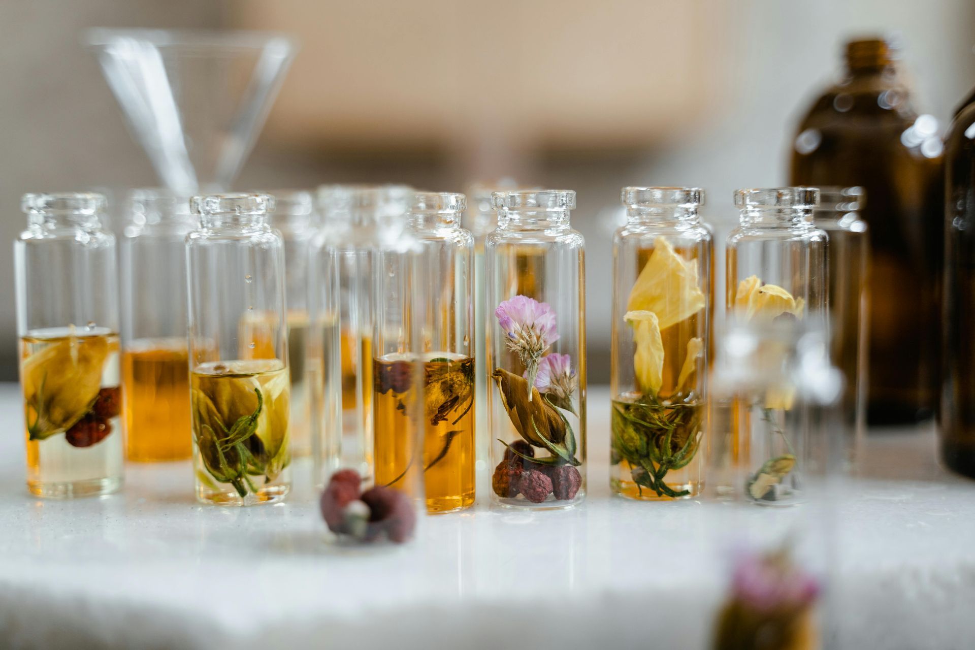 Frascos de vidro cheios de líquido dourado e flores variadas,
