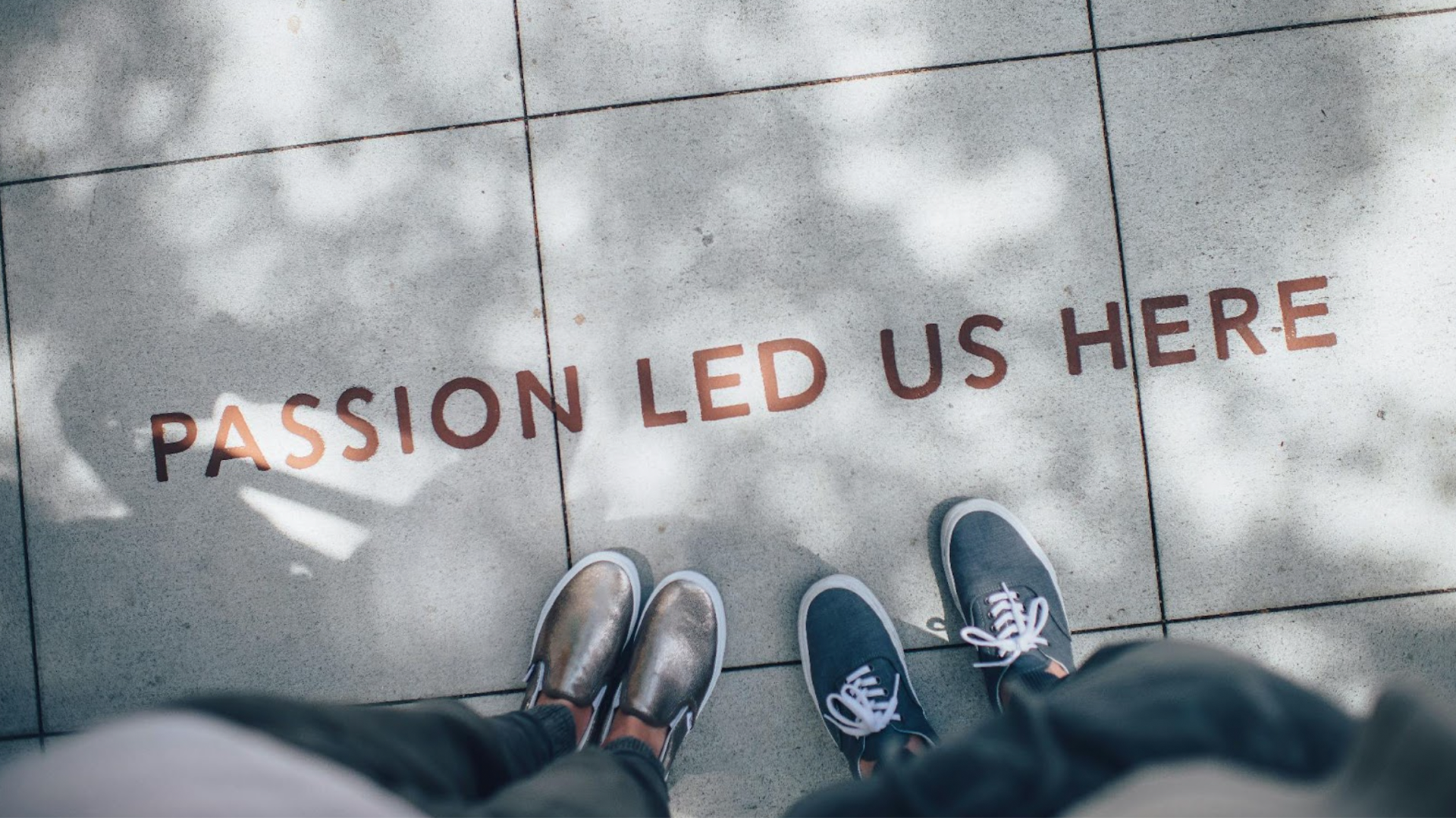 A couple of people standing next to each other on a sidewalk with the words `` passion led us here '' written on the ground.