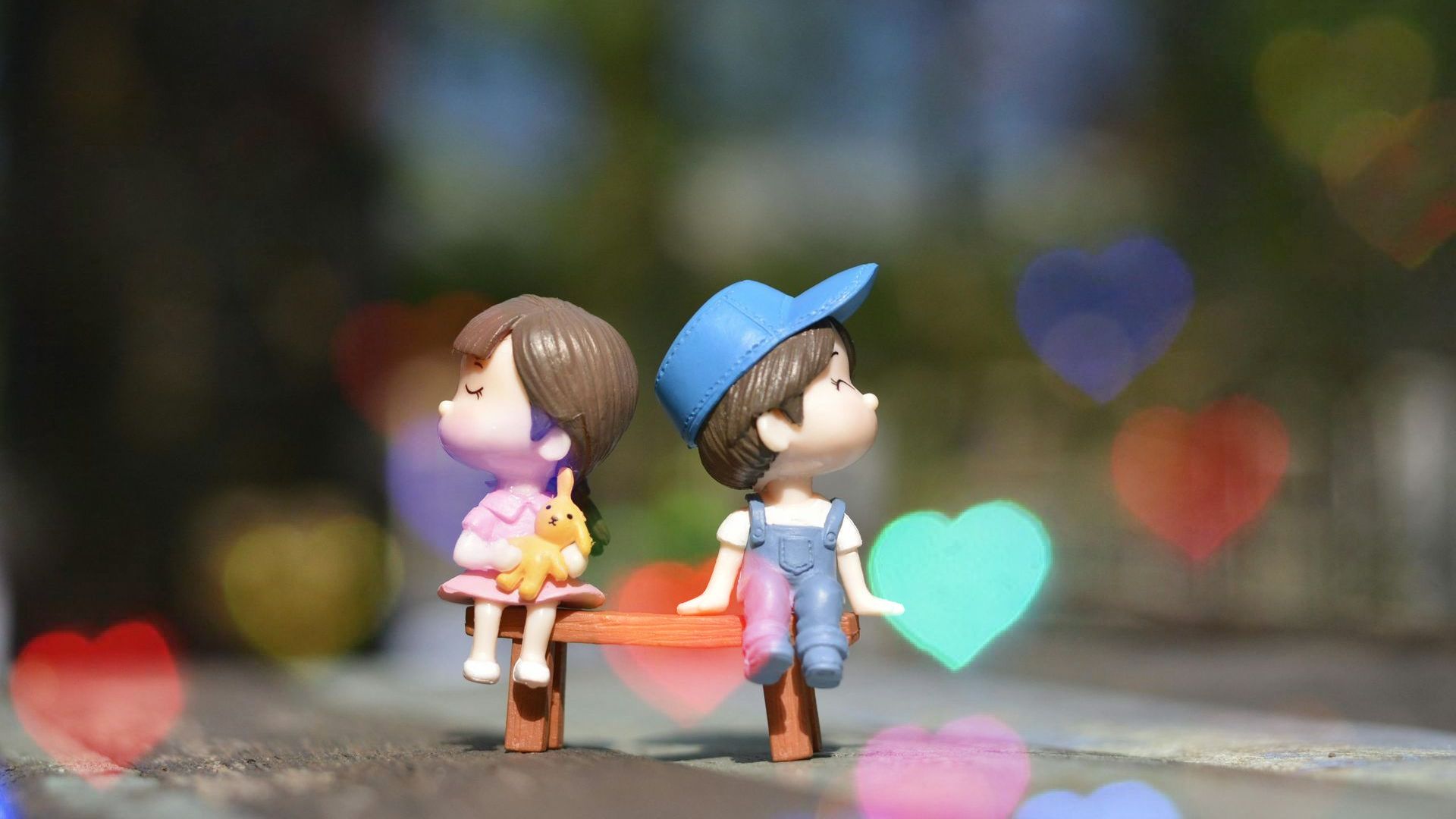 A boy and a girl are sitting on a bench with hearts in the background.