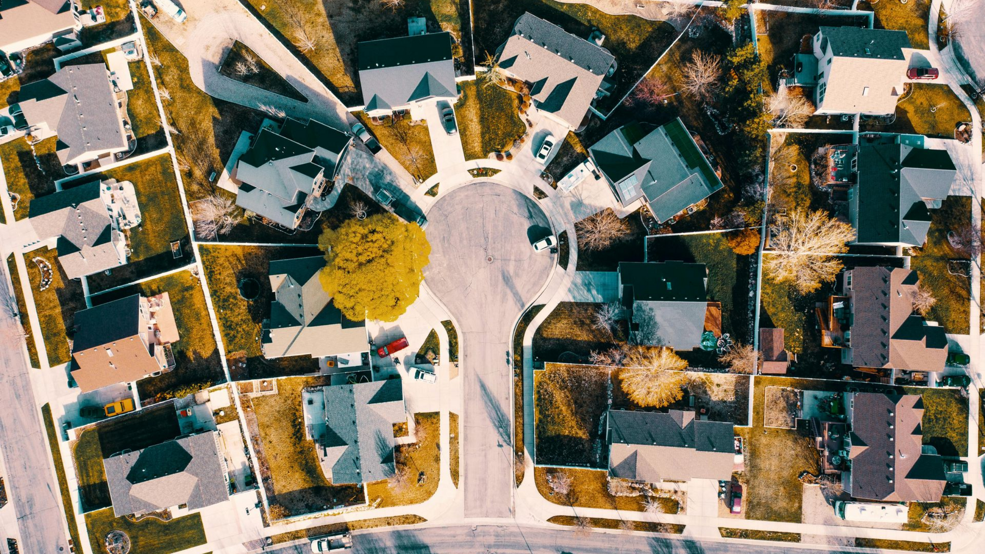 Aerial view of suburban neighborhood with houses surrounding a roundabout, autumn colors.