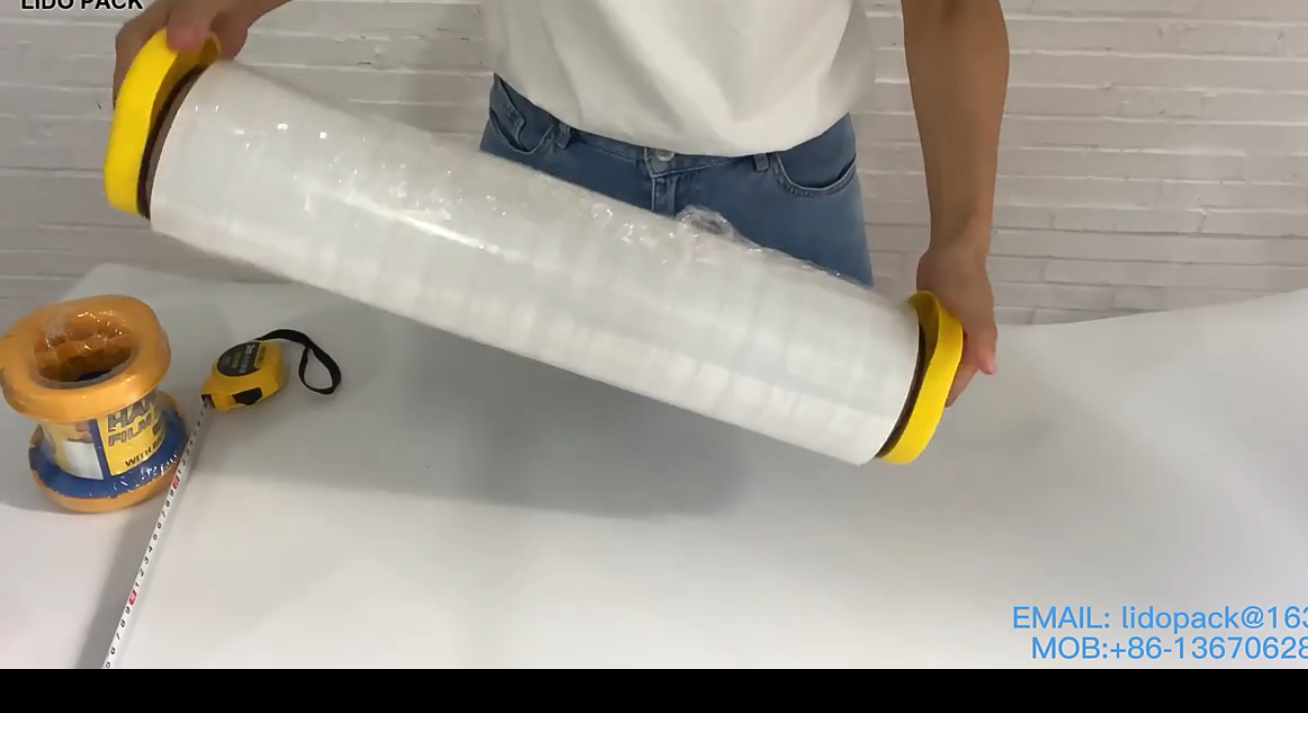 Una persona sostiene un tubo grande de plástico transparente con extremos amarillos sobre una mesa blanca, con cinta adhesiva cerca.