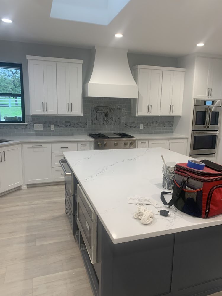 Bright modern kitchen with white cabinets, large island, and a red tool bag on the counter