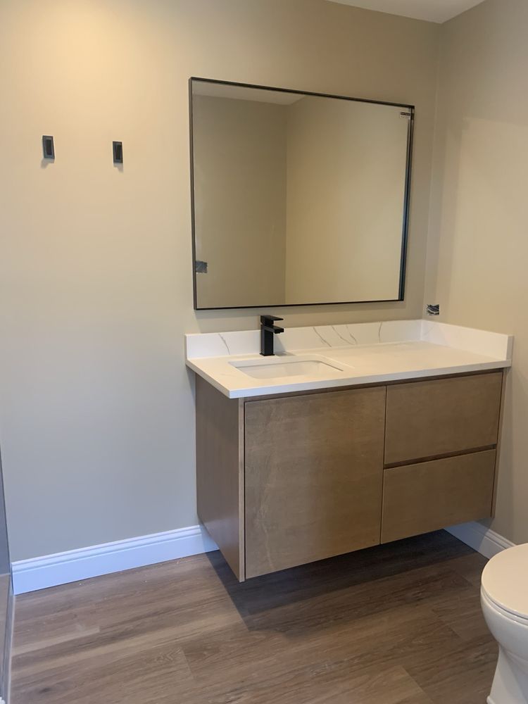Modern bathroom vanity with mirror, white countertop, and wood cabinet against a beige wall.
