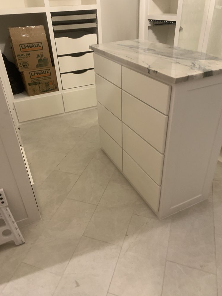 White drawer island with marble top in a bright walk-in closet with tiled floor.