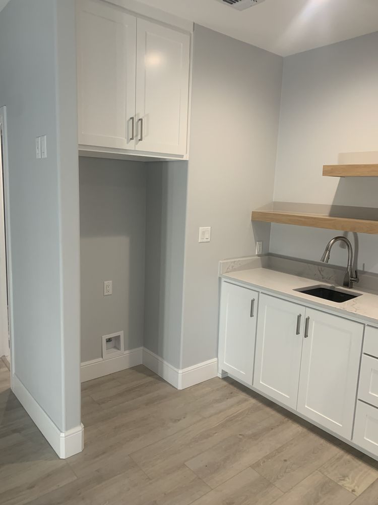 Small kitchen nook with white cabinets, open shelving, sink, and light wood flooring.