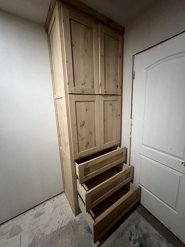 Tall wooden cabinet with three open drawers in a small hallway beside a white door.
