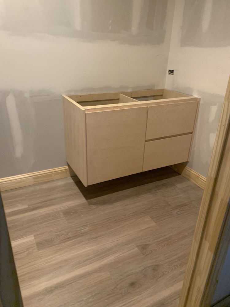 Small unfinished bathroom with a light wood vanity and double sink against a white wall.