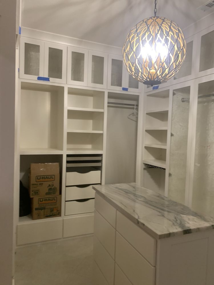 White walk-in closet with built-in shelves, drawers, hanging space, and a marble island under a pendant light.