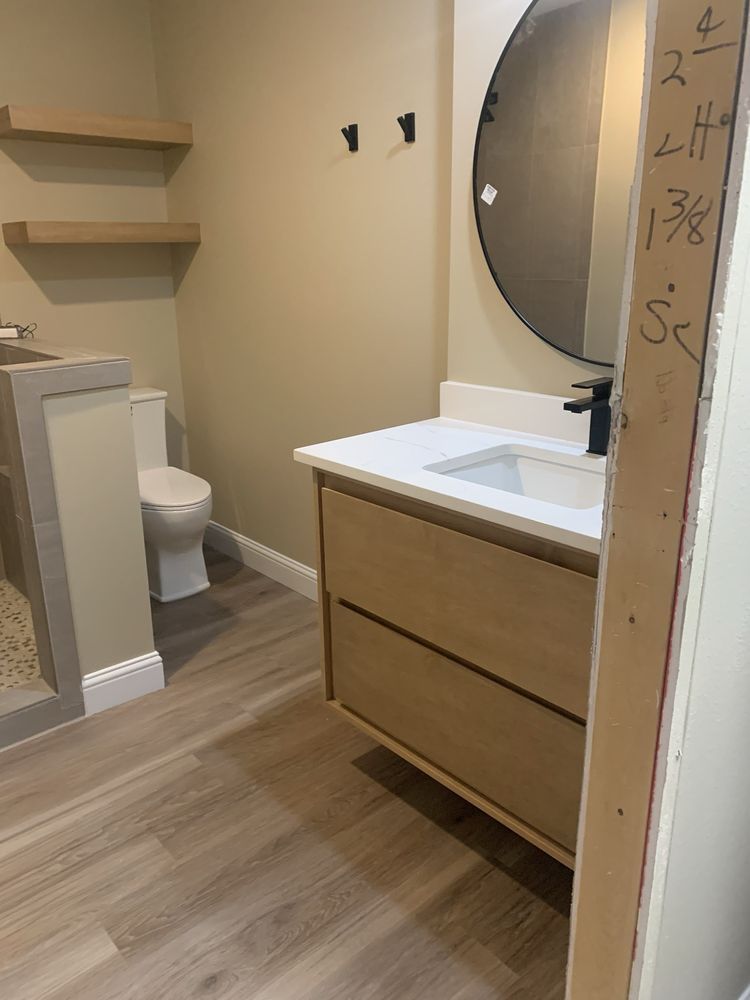 Small modern bathroom with vanity, round mirror, toilet, and wall shelves.
