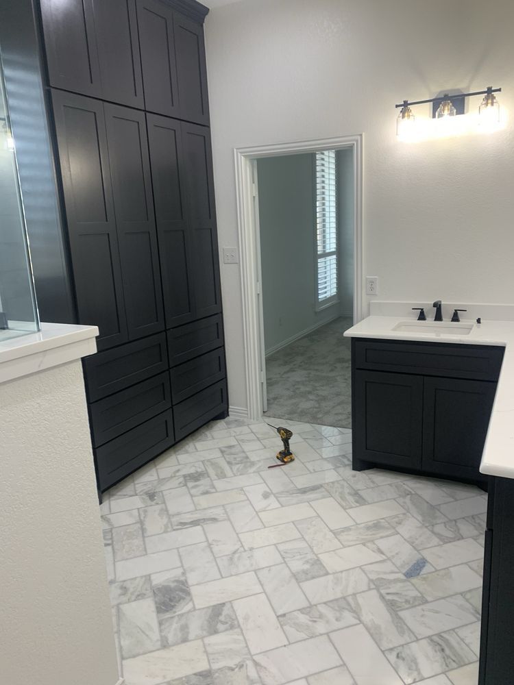 Modern bathroom with tall black cabinets, white vanity, light tile floor, and walk-in shower.