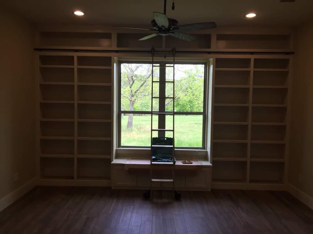 Empty room with built-in shelves, a window seat, and a large central window overlooking trees