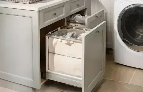 Pull-out laundry hamper in a white cabinet next to a washing machine