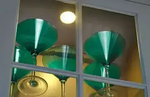 Green hanging pendant lamps behind a window with a ceiling light reflected above