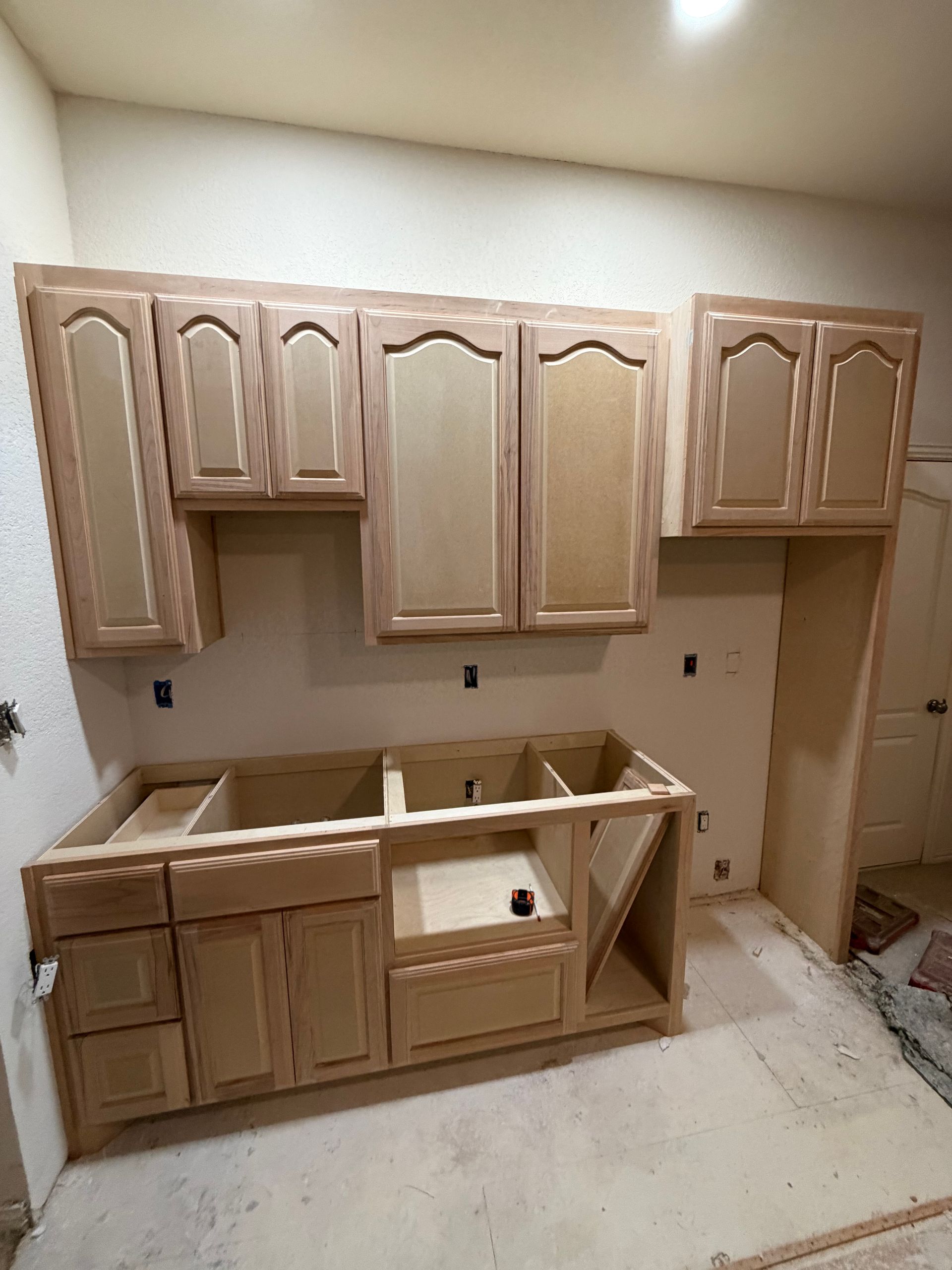 Partially installed beige kitchen cabinets in a room under renovation