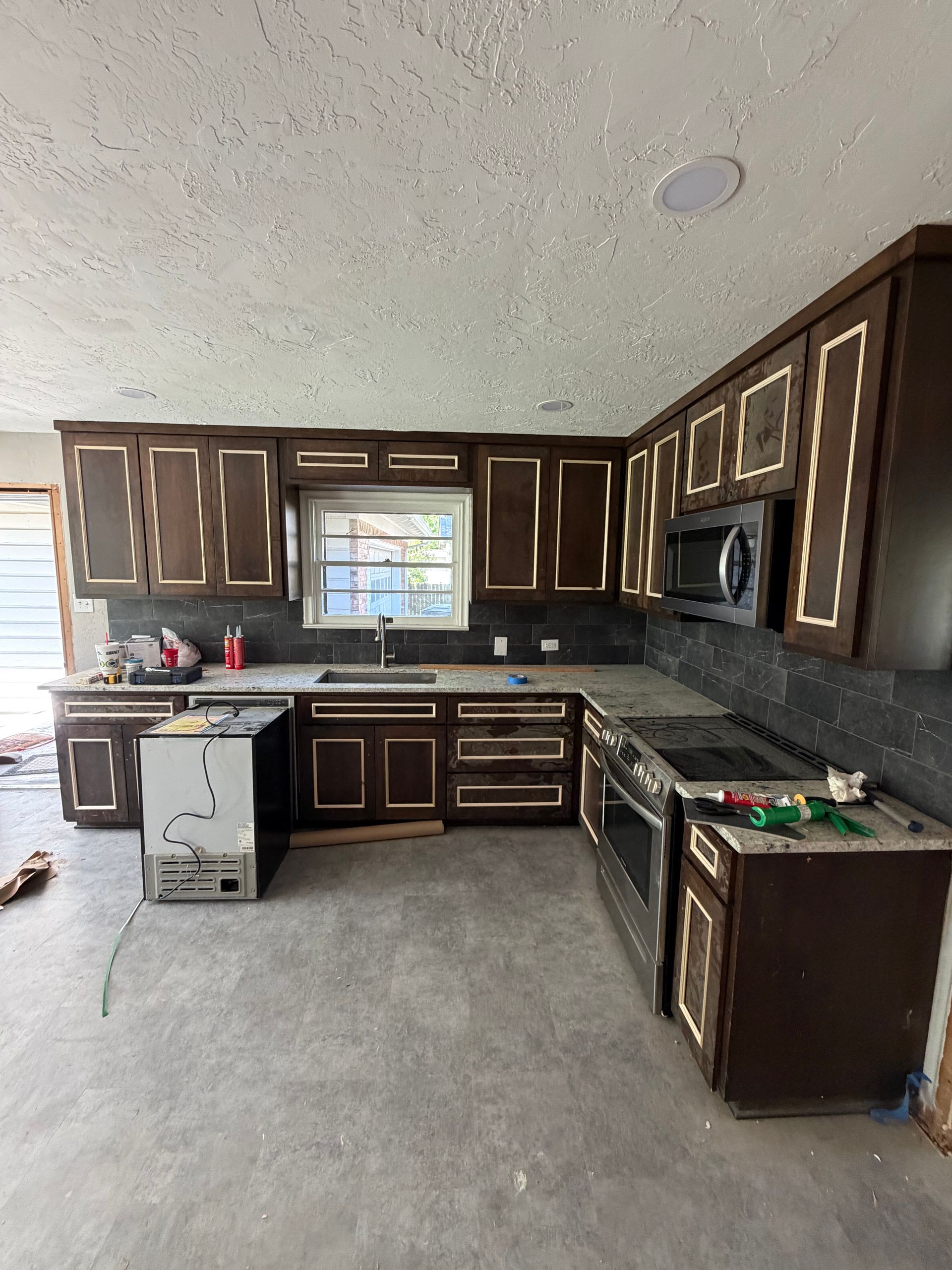 Empty kitchen with dark wood cabinets, black countertops, and a gray floor under renovation.