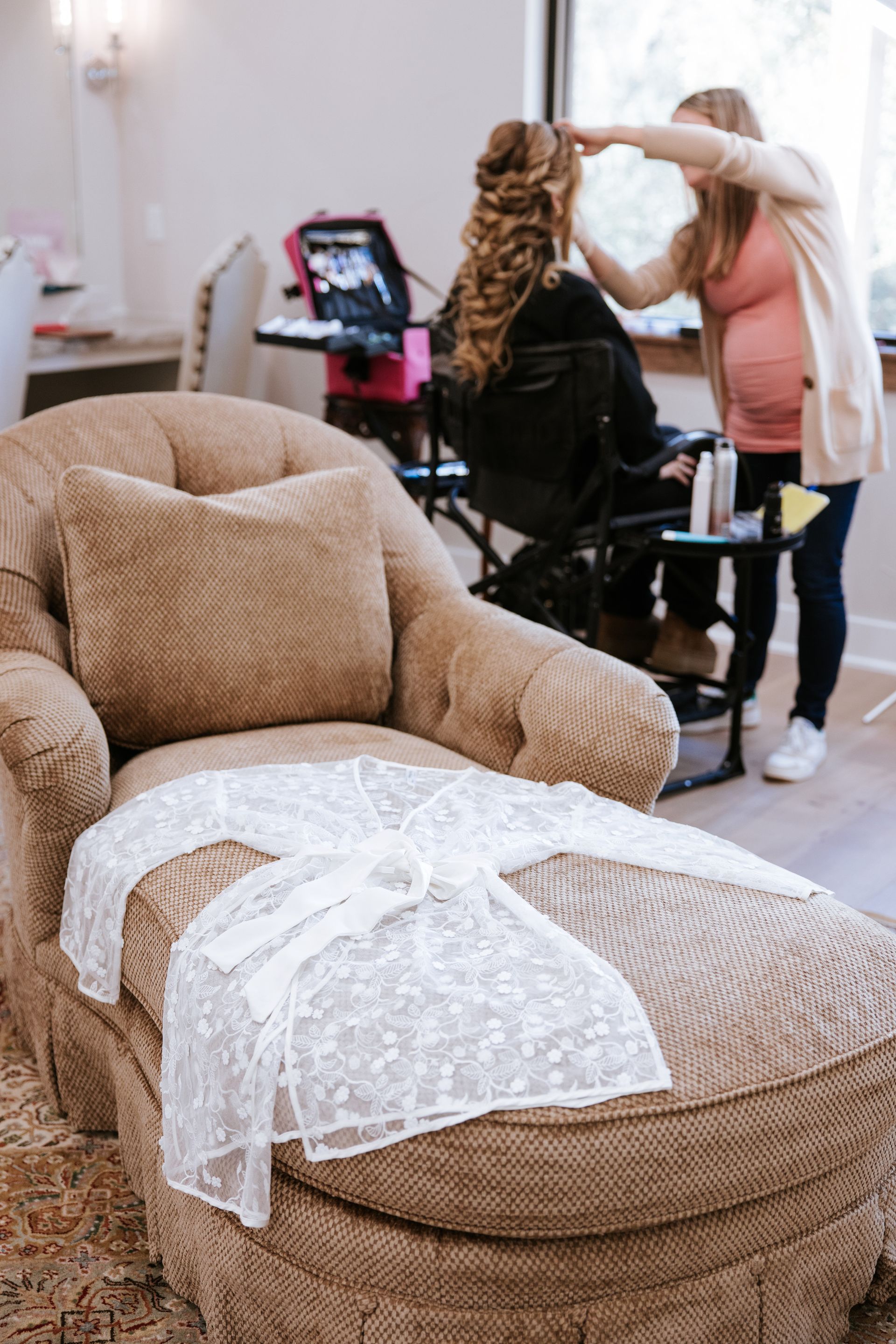 Lace robe on chaise lounge; woman's hair styled by stylist in well-lit room.