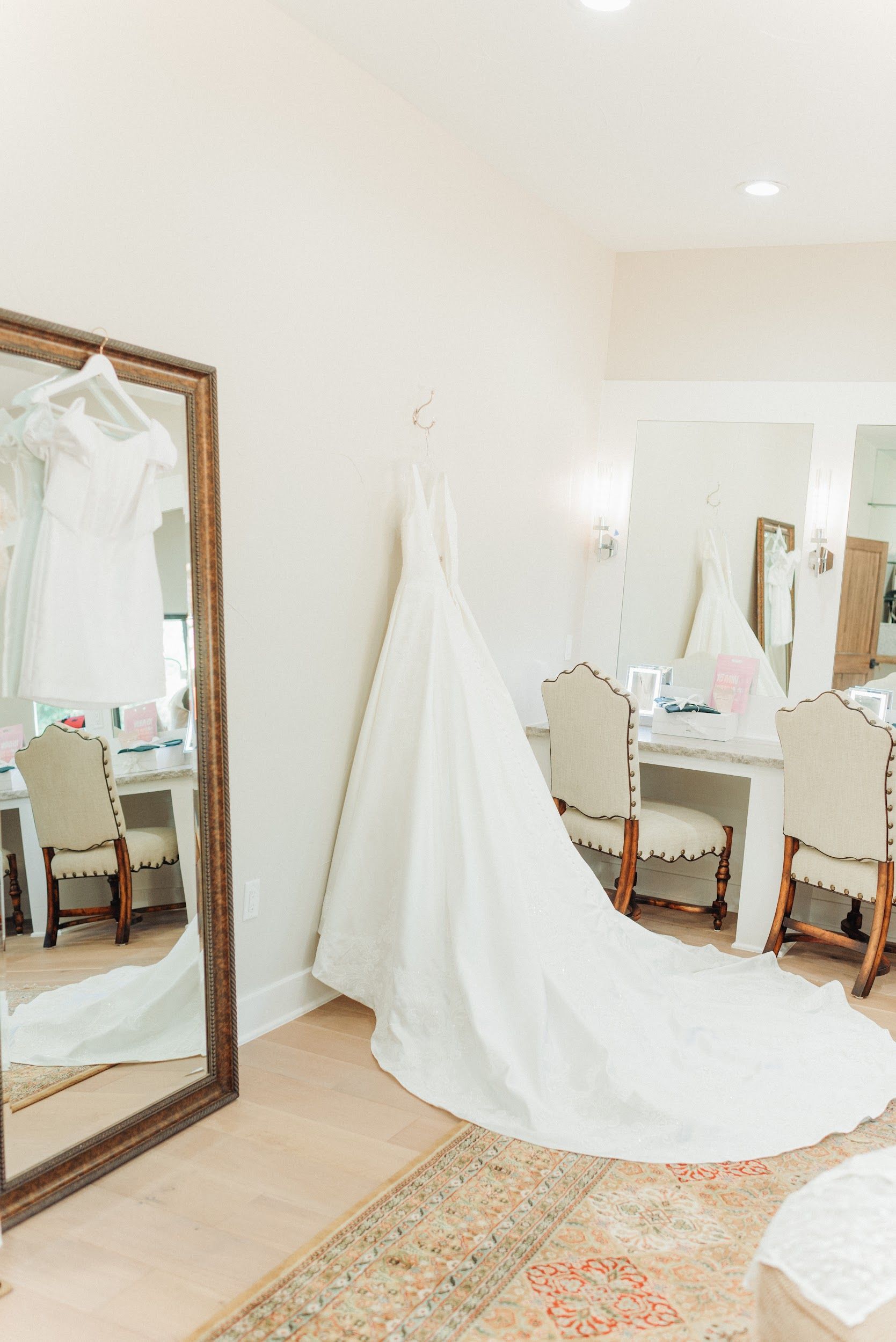 Wedding dress hanging on a wall in a bridal suite, with a long train and mirror reflection.