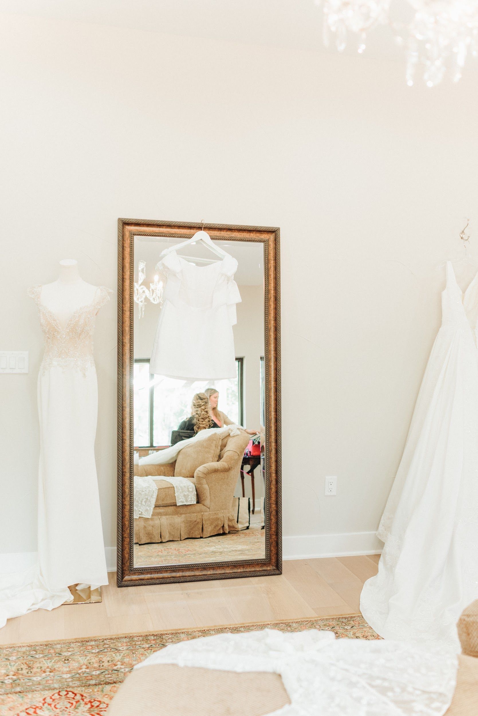 Wedding dresses displayed in a bright room with a large mirror reflecting a person.