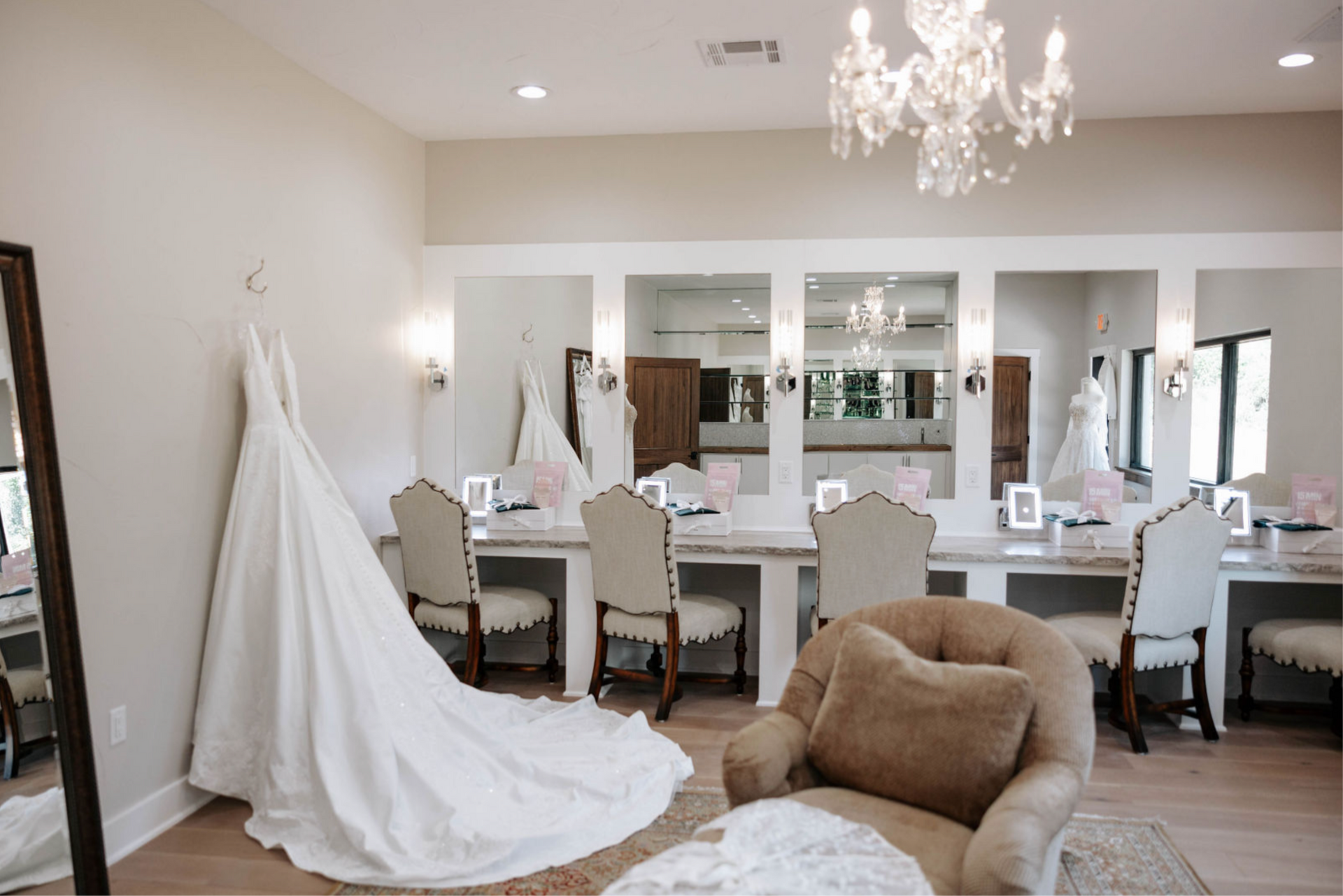 Bridal shop dressing room with gowns hanging and illuminated vanities; an armchair is in the foreground.