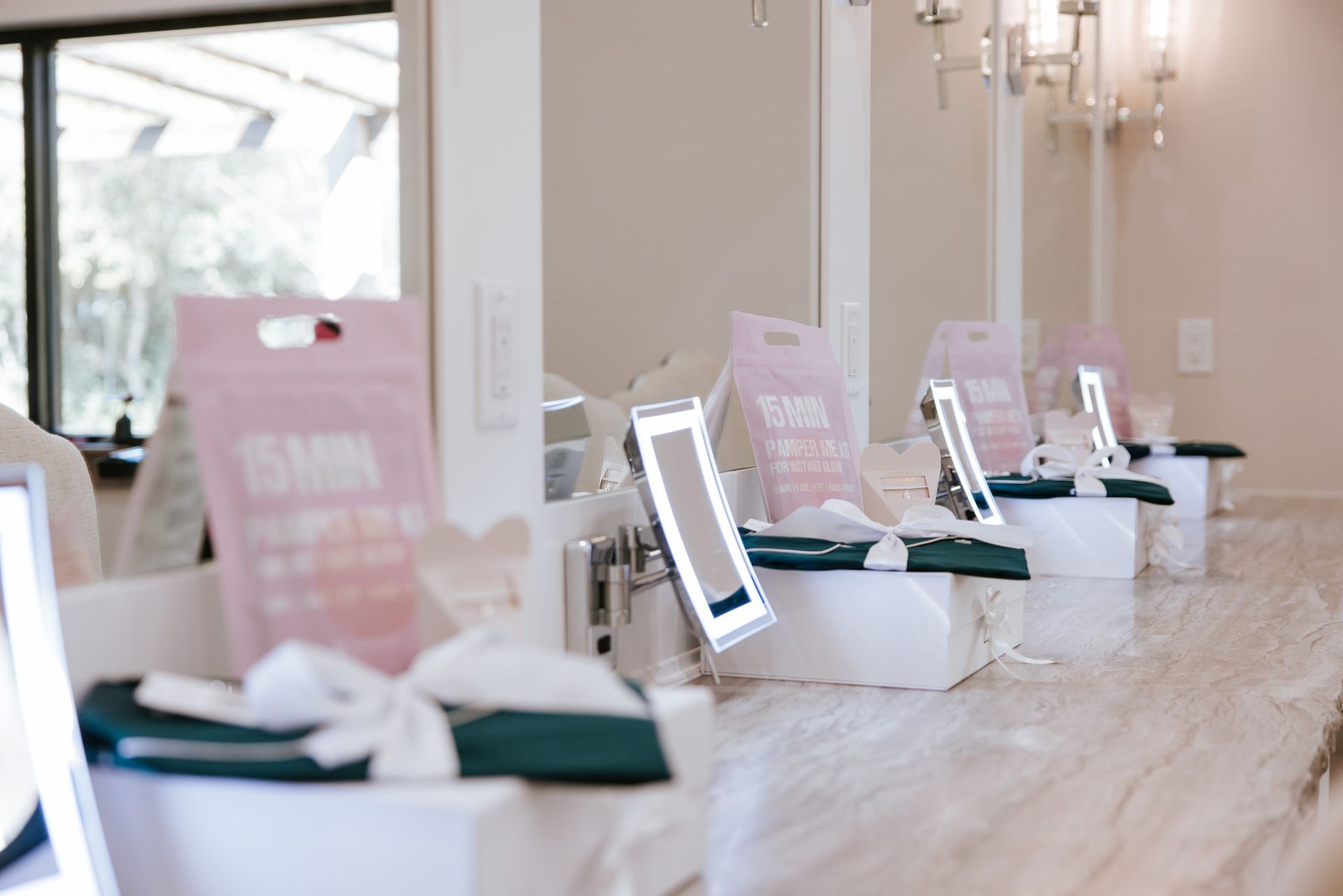 Row of makeup stations with mirrors, pink signs, and green cloths on white boxes.