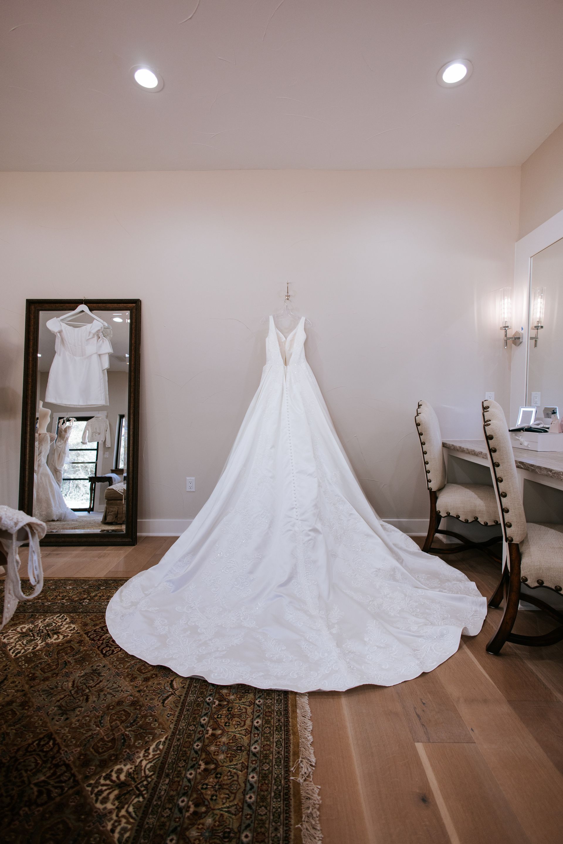 A long white wedding dress hanging on a wall, with a train spread on the floor.