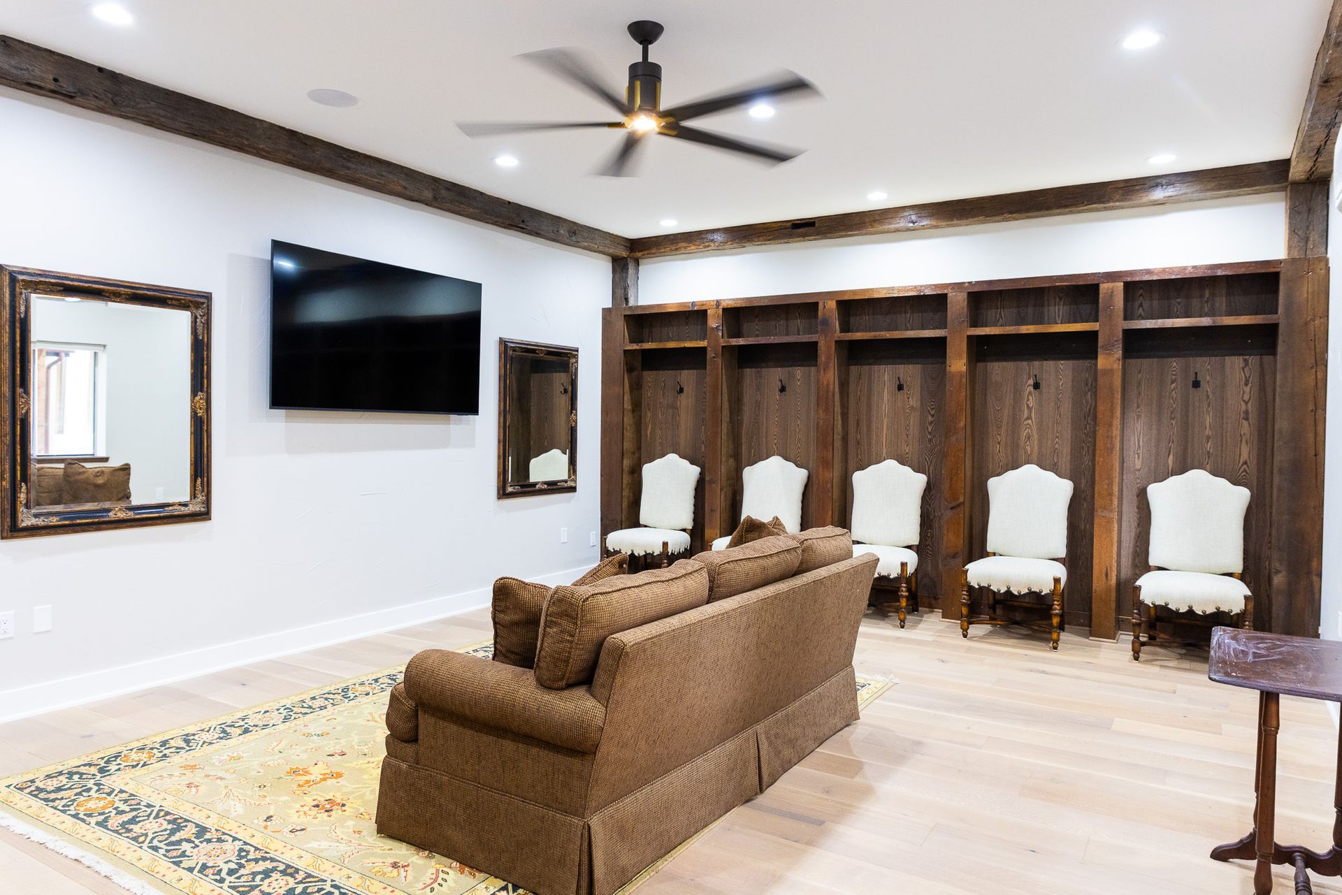 A well-lit room featuring a seating area, TV, wooden lockers, mirrors, and chairs.