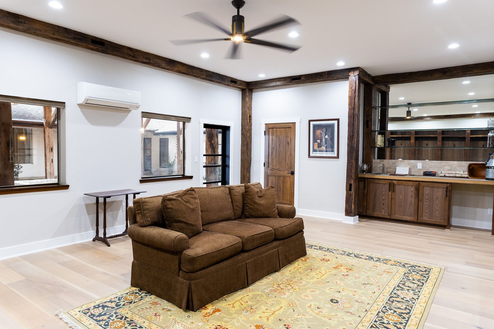 Cozy living room with brown sofa, wooden beams, windows, and a rug.