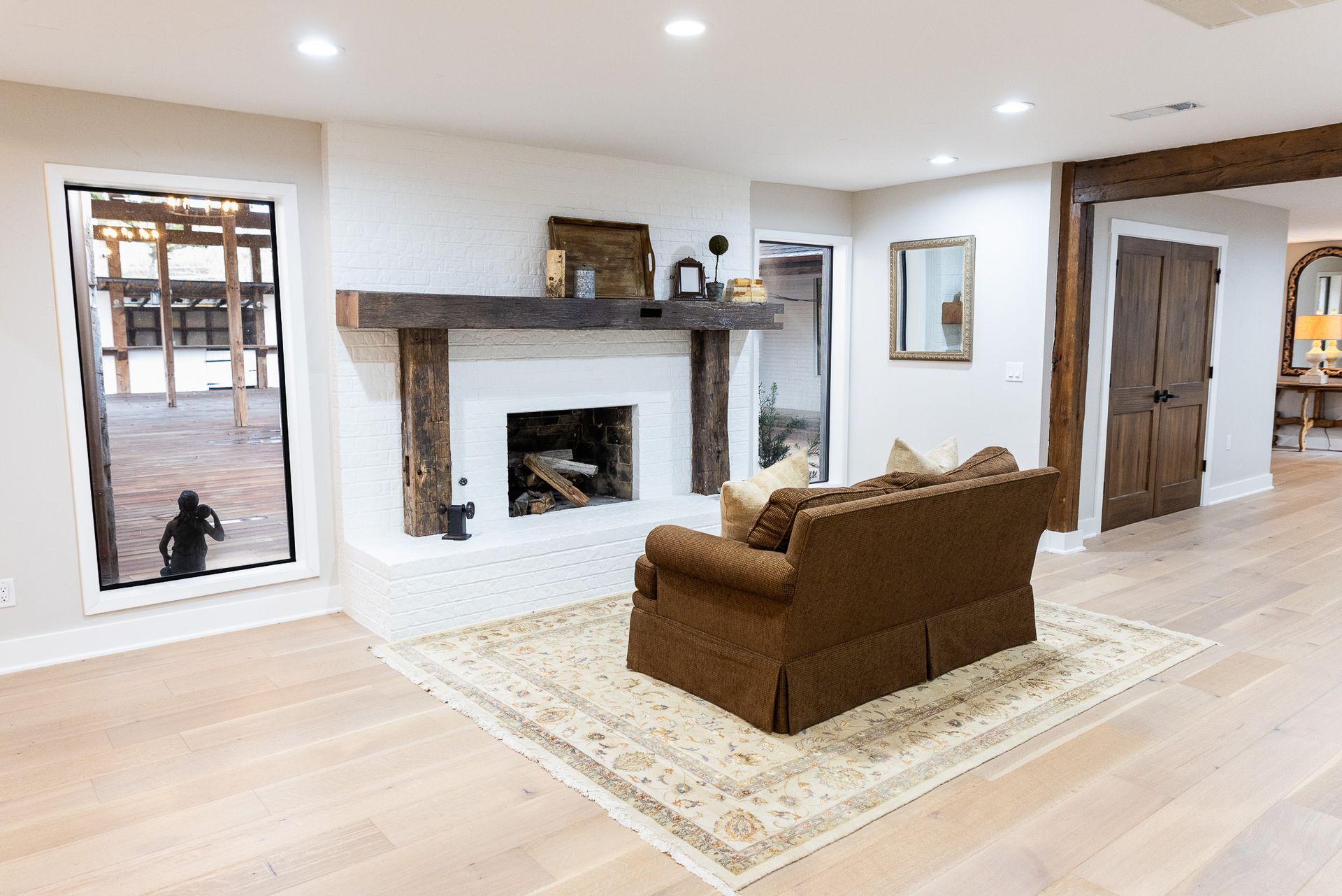 Living room with a fireplace, sofa, rug, and large windows. Warm-toned wood accents and light-colored walls.