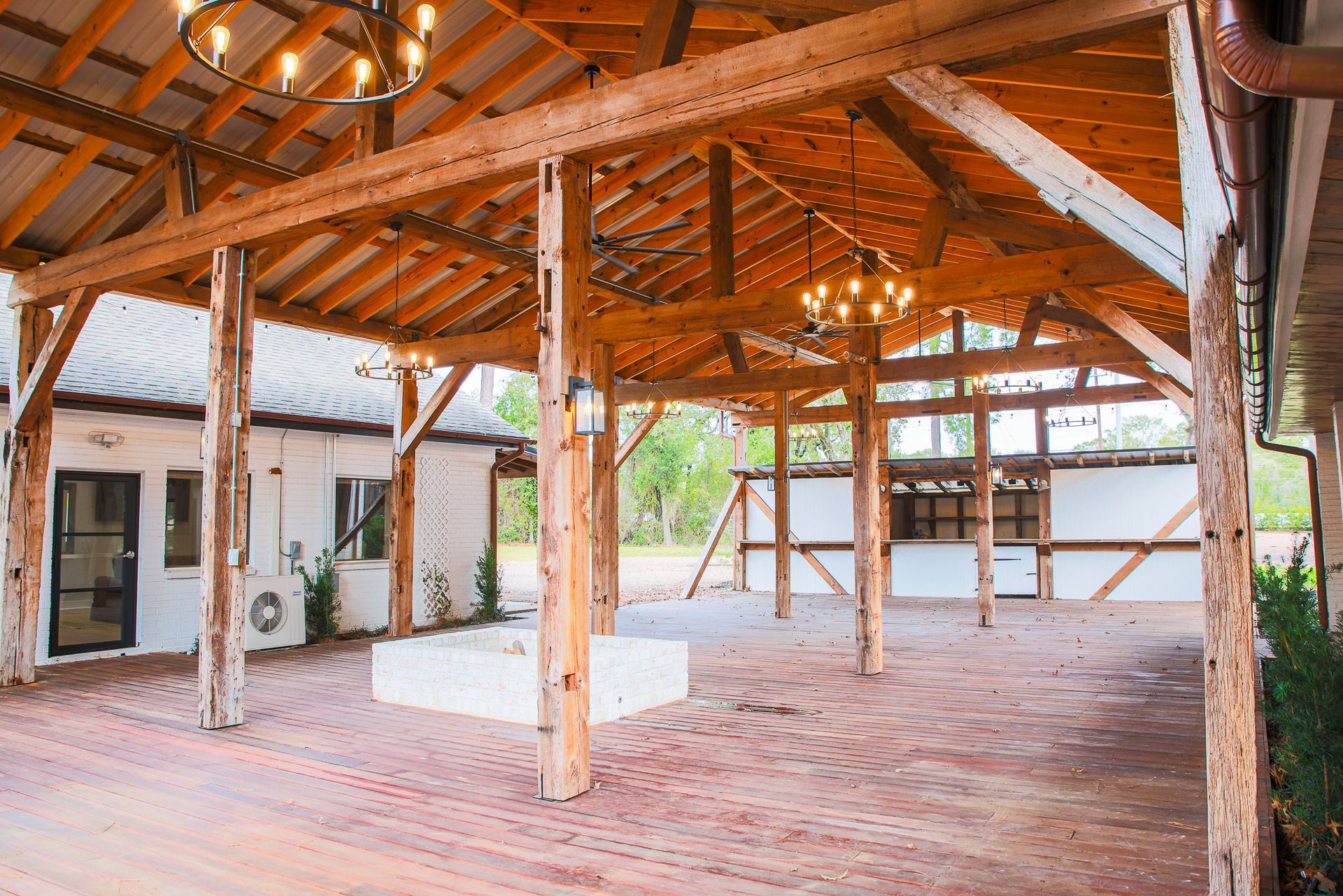 A covered outdoor patio with wooden beams and a red brick floor, with lights and a white building.