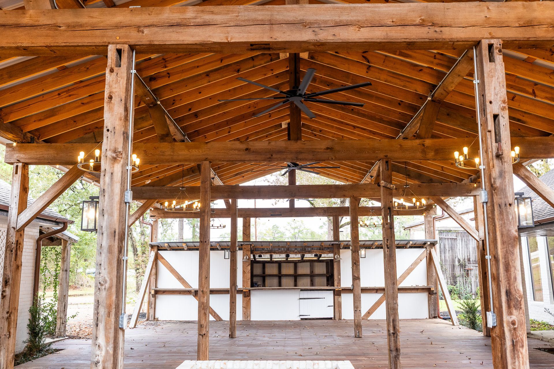 Wooden-beamed event space with string lights, open sides, and a bar area in the background.