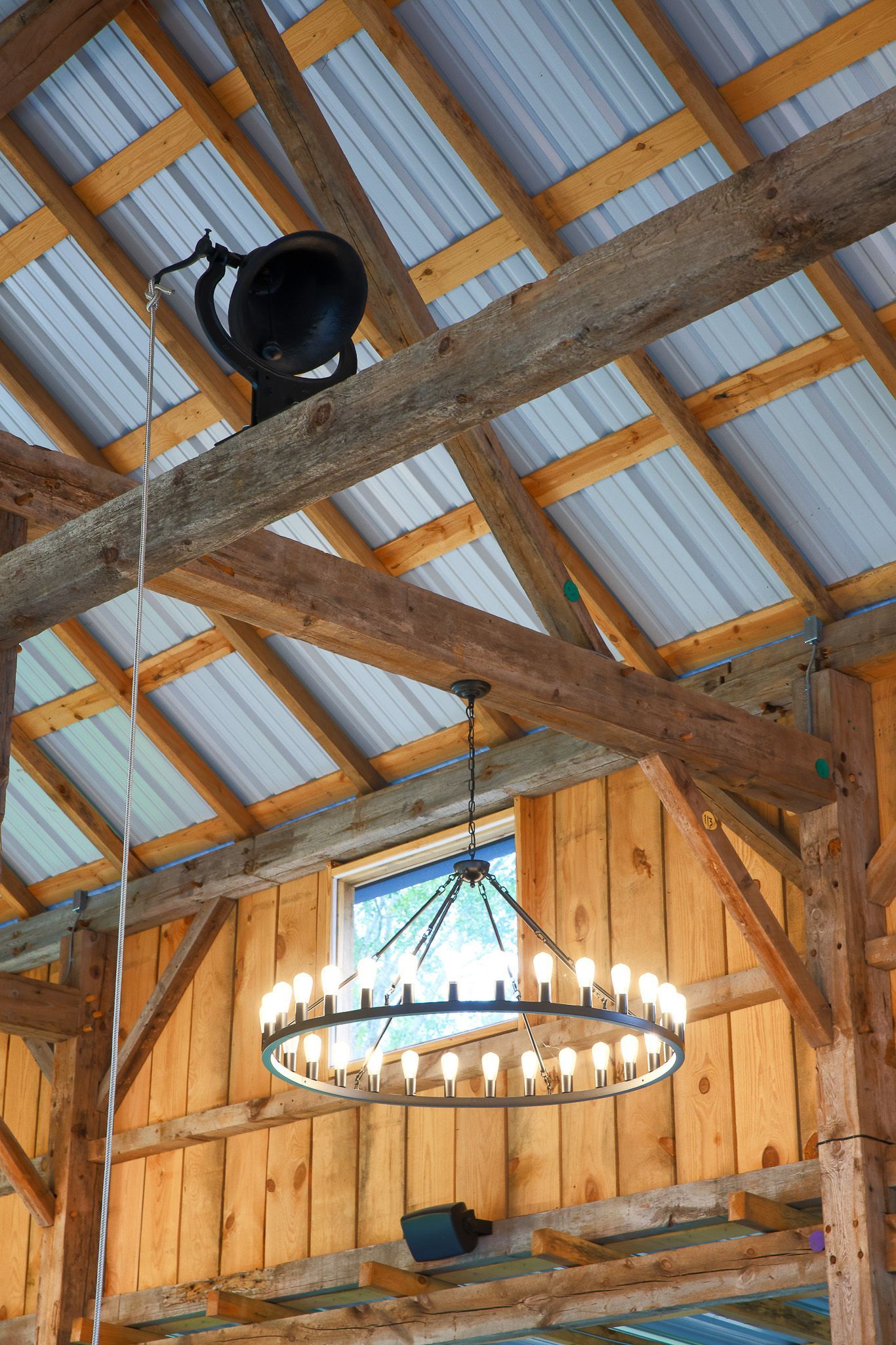 Wooden barn interior with a chandelier and speaker hanging from the ceiling.