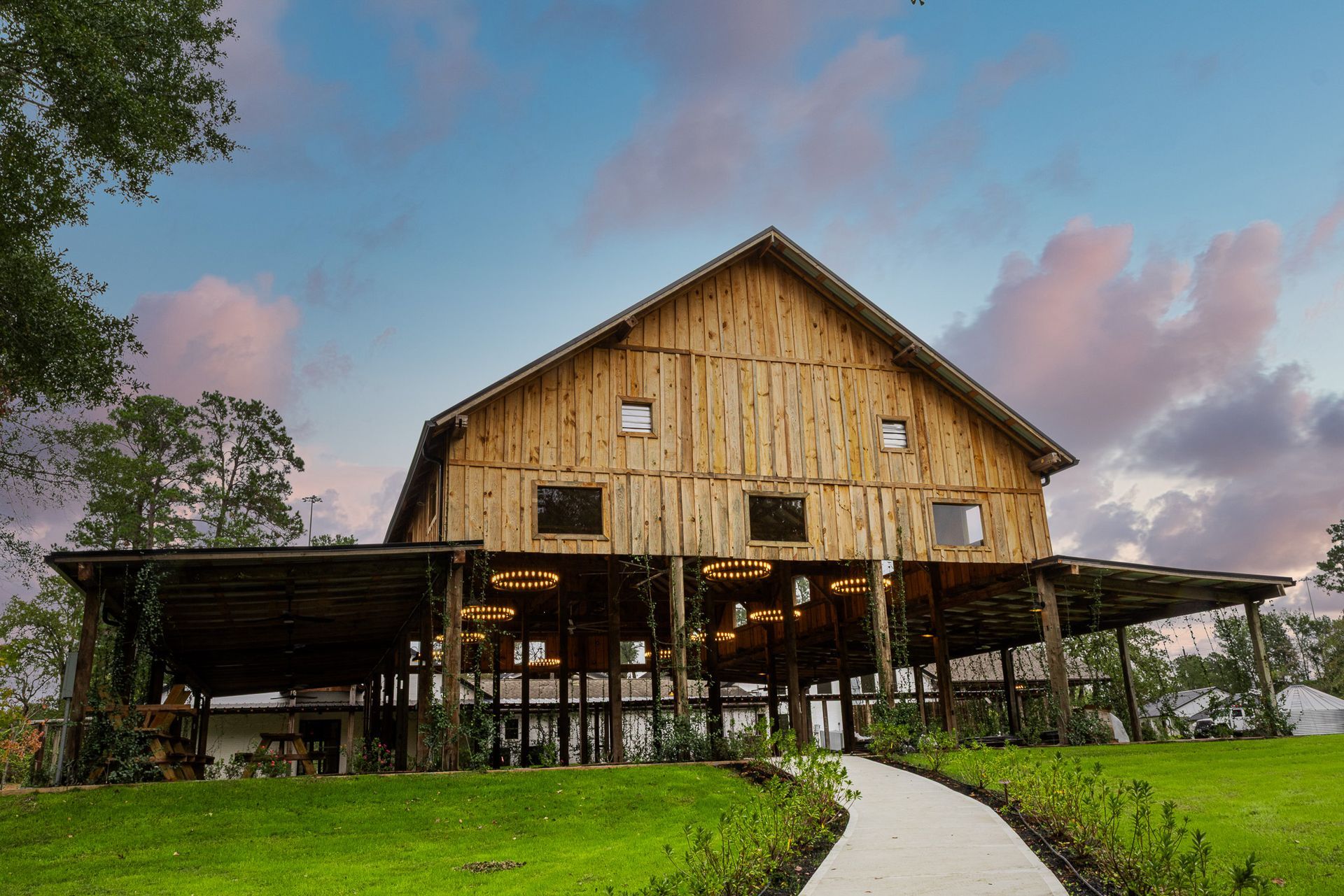 Rustic wooden barn with a covered porch and grassy lawn under a colorful sunset.