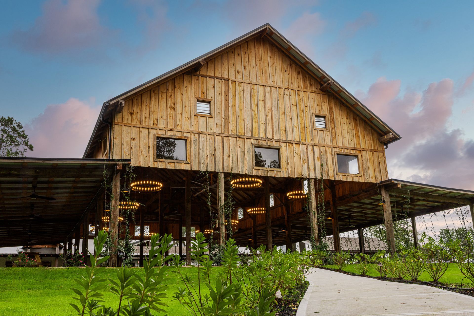 Wooden barn venue with open-air lower level, path leading to it, and a dusk sky.