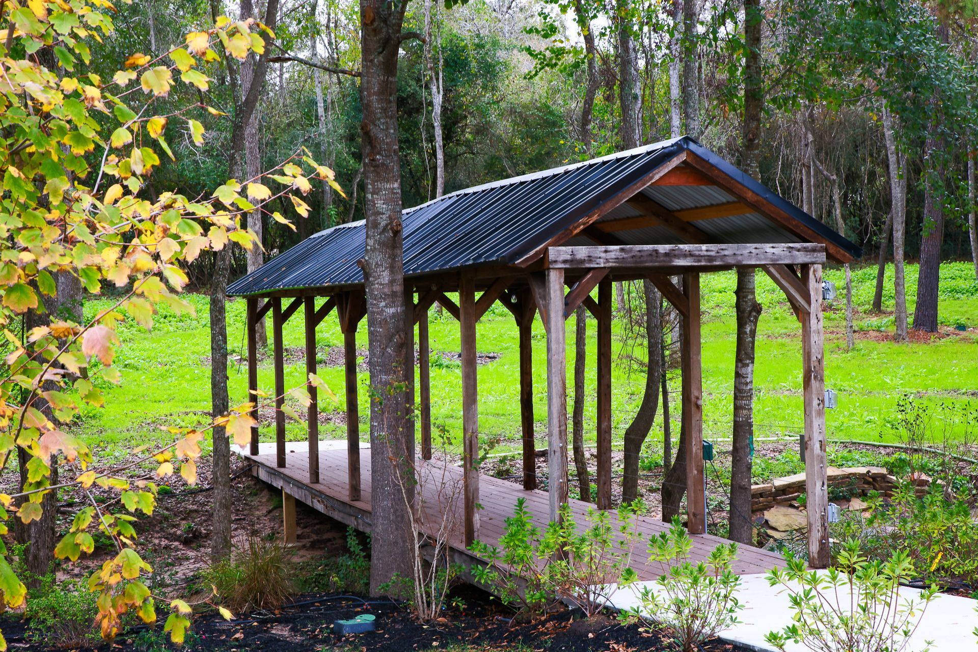 Covered wooden bridge with a gray roof over a small stream in a park.