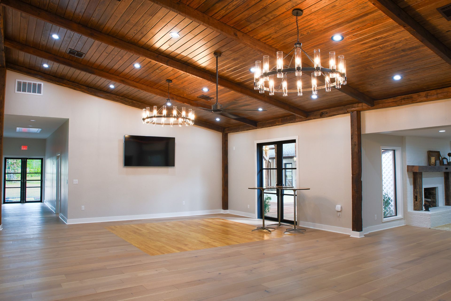Large room with wooden ceiling and chandeliers, light wood floor, and two doorways.