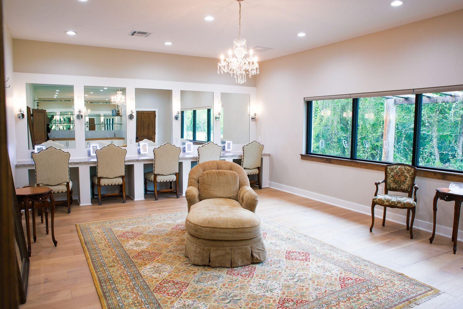 Elegant dressing room with makeup stations, large rug, and chandelier.