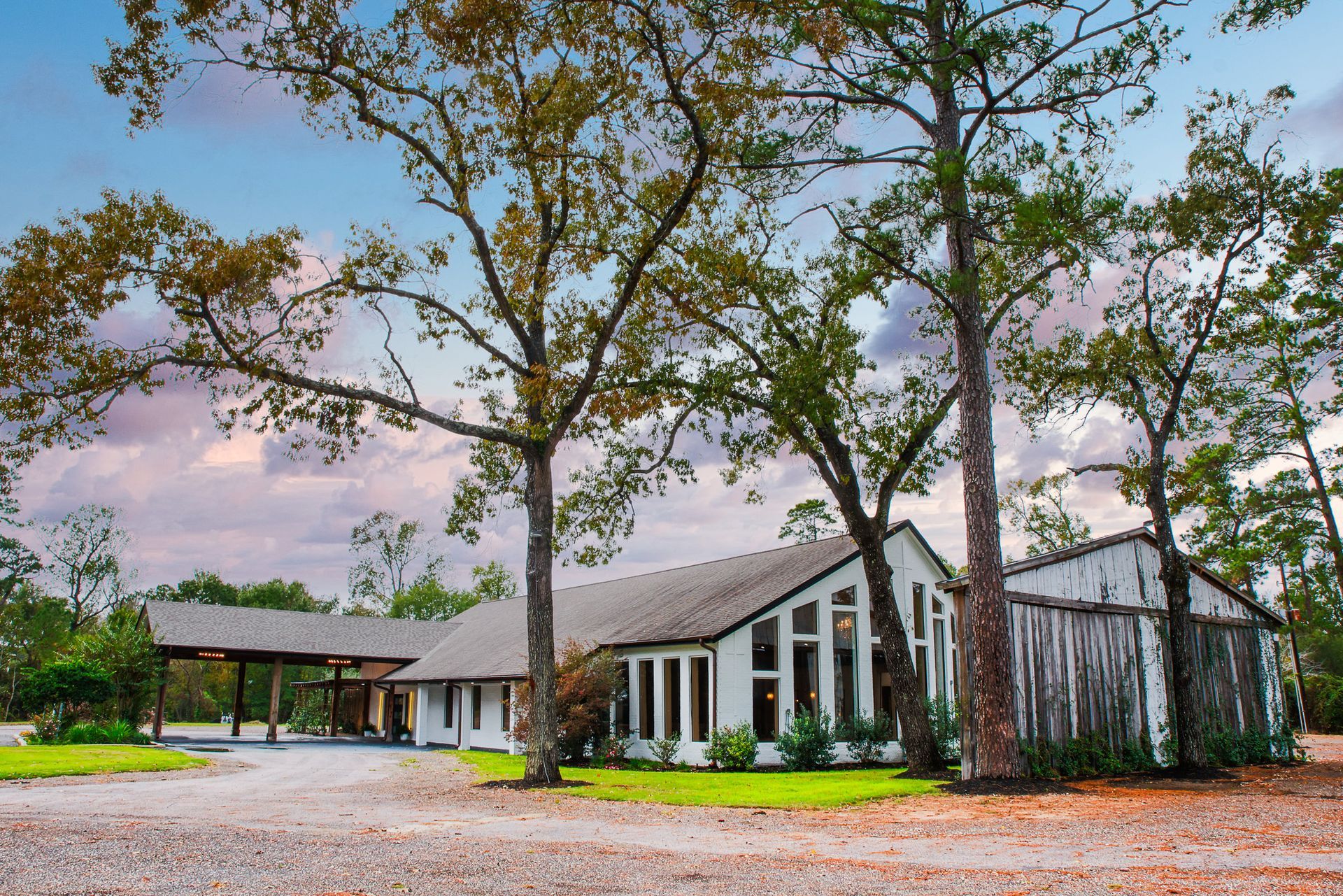 White building with large windows, surrounded by trees under a cloudy sky.