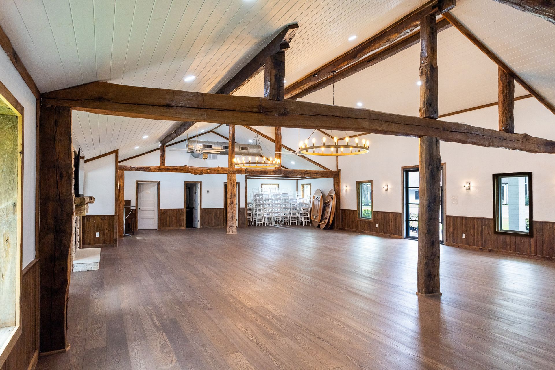Spacious wooden-floored event hall with exposed beams, windows, and decorative lighting.