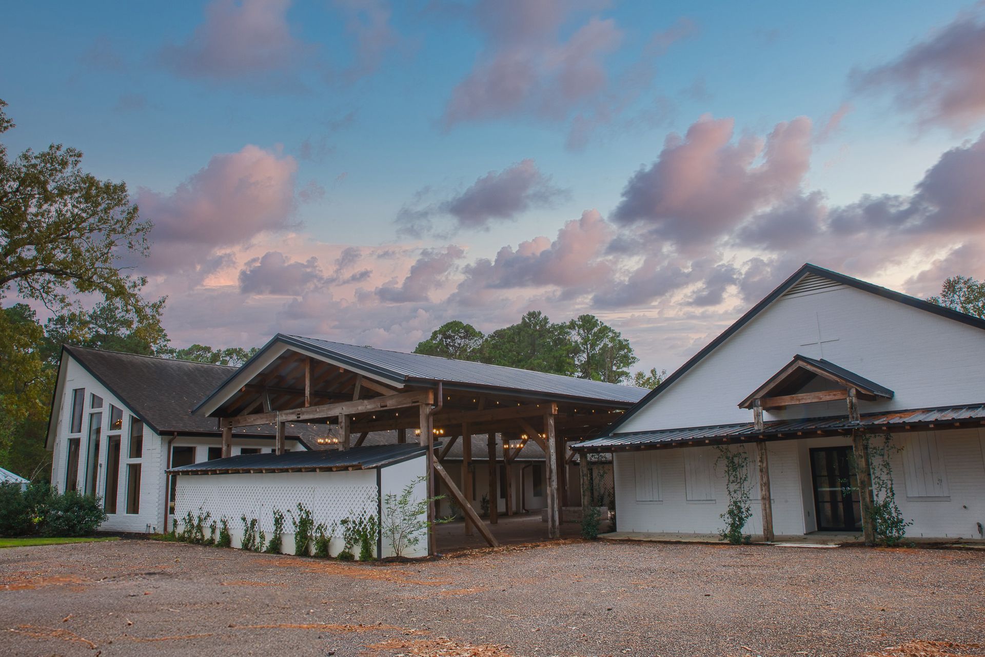 White building with exposed wood beams and a gravel driveway, under a cloudy, colorful sky.