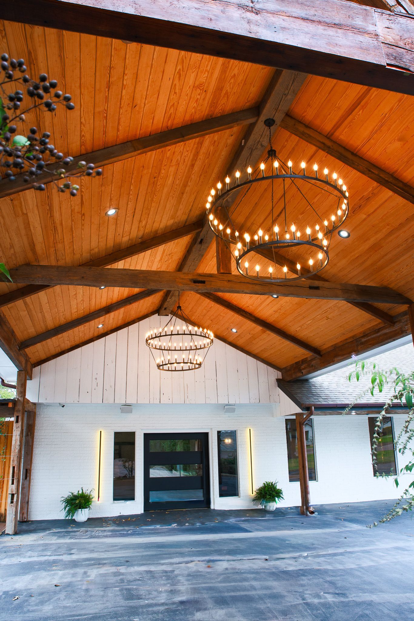 Covered entrance with wood ceiling, chandeliers, and white facade.