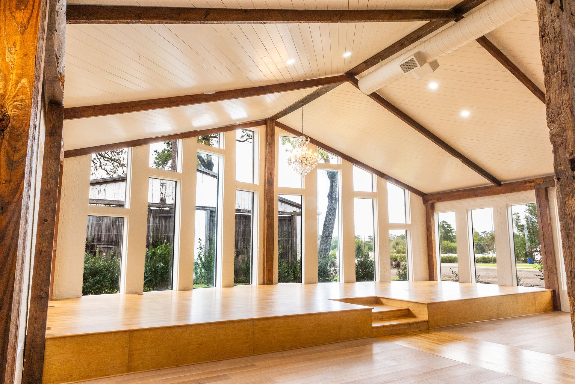 Wooden-floored event space with large windows, stage, and exposed beams; interior view.