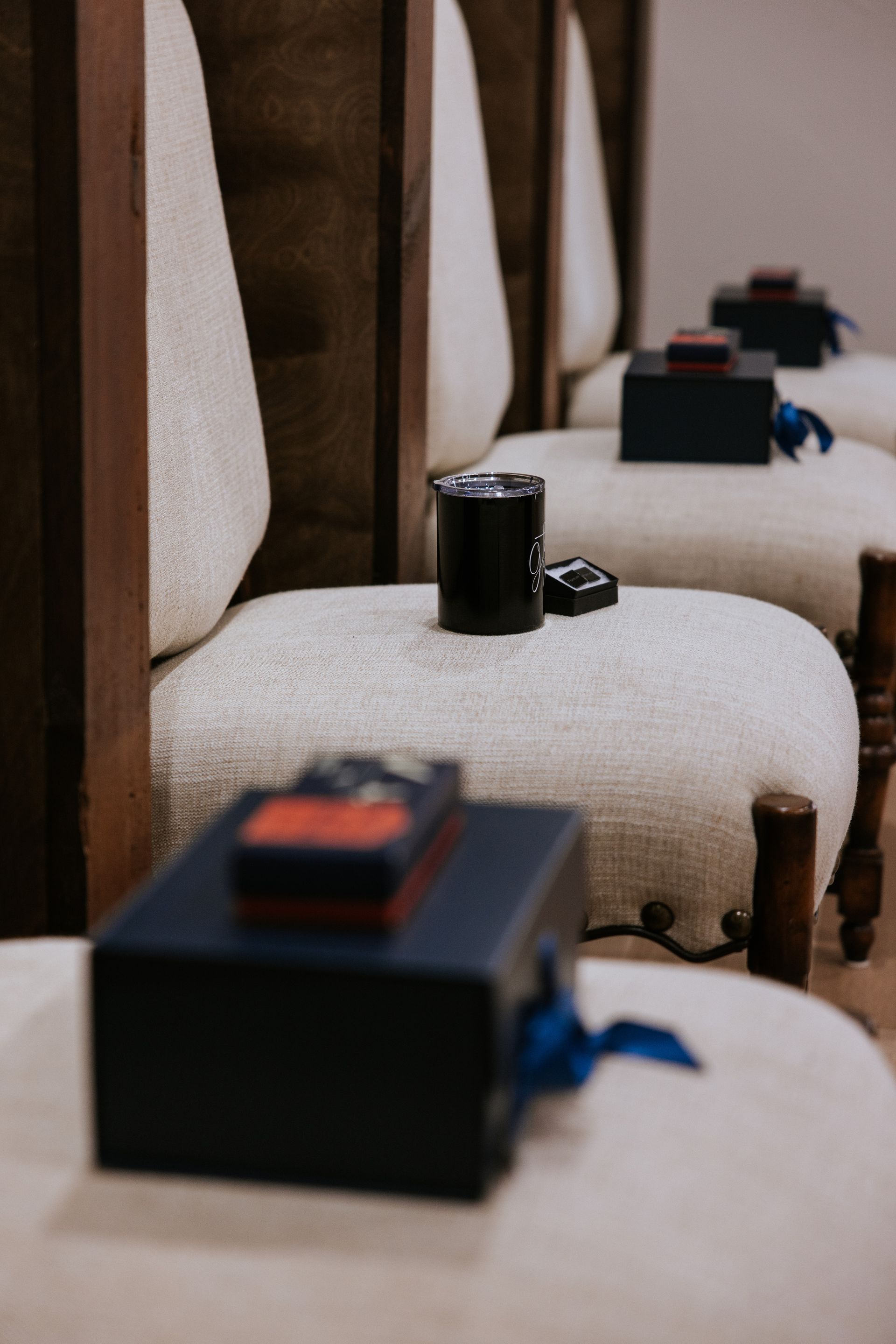 Row of upholstered chairs, each with a black box, a tumbler, and a remote control on the seat.